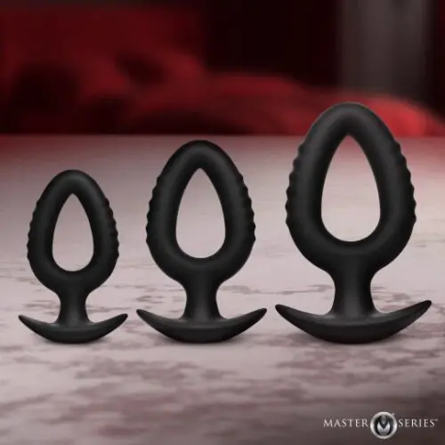 Three black silicone butt plugs of different sizes on a surface.