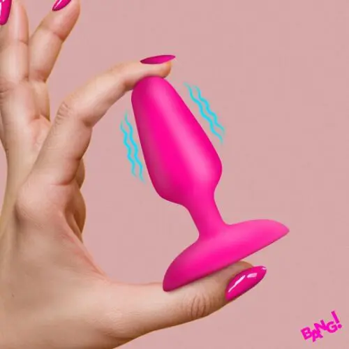 Hand holding a small pink silicone butt plug against a pink background.
